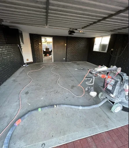 Before: bare concrete mid-grind with the diamond grinder and vacuum hoses